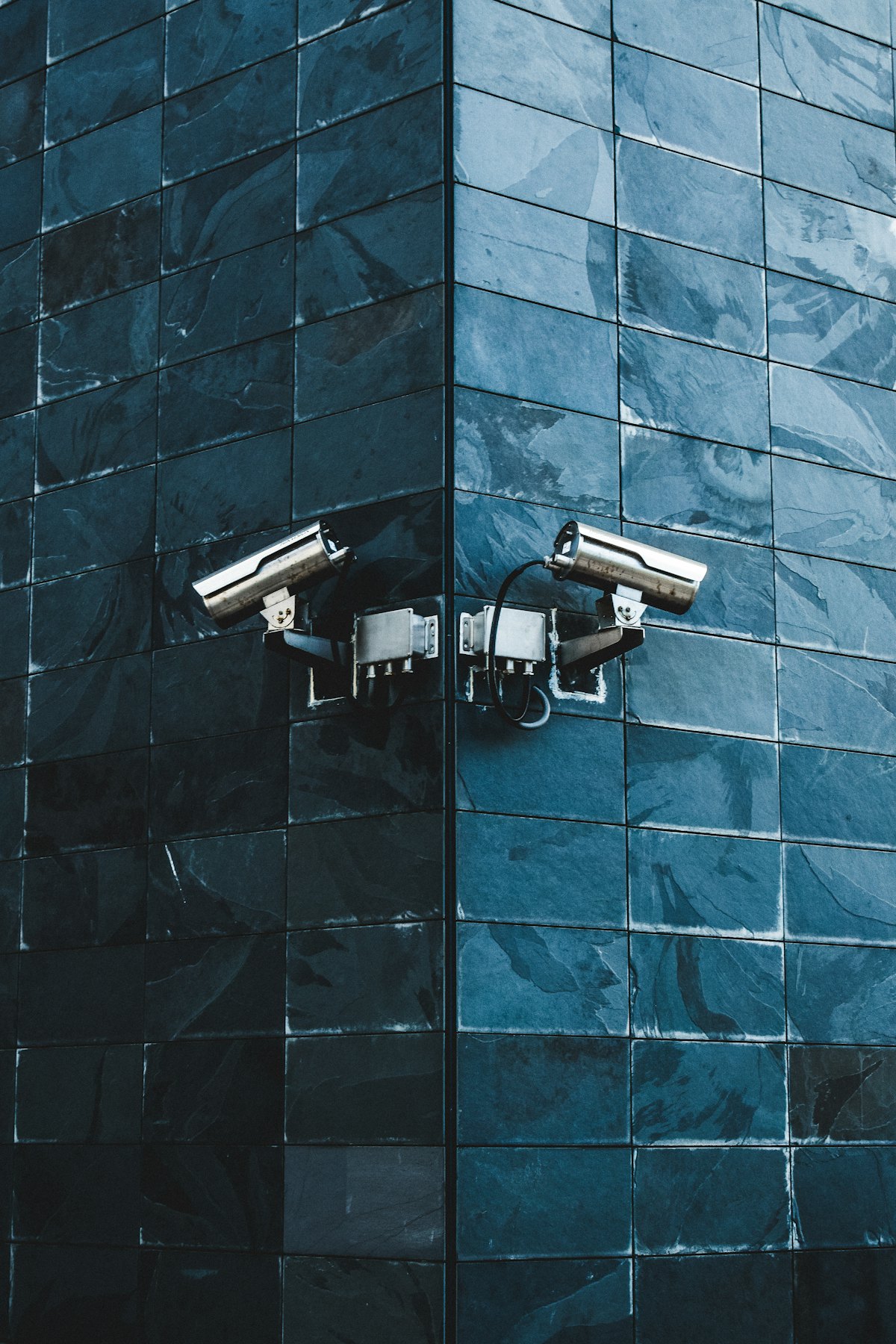 Two security cameras mounted on a dark blue tiled wall